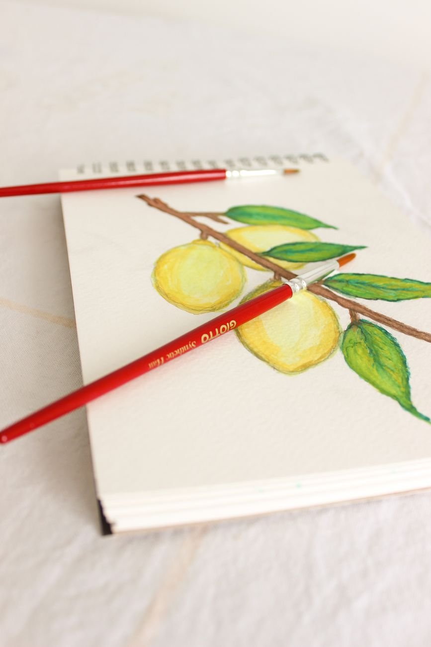 Vibrant lemon illustration in a sketchbook with two paintbrushes on paper