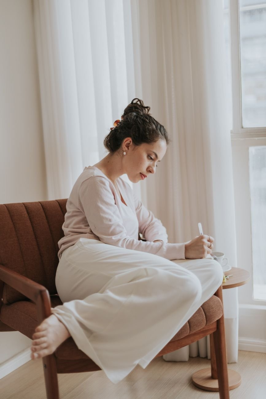 A woman enjoying a peaceful moment journaling while sitting in a cozy chair by a window