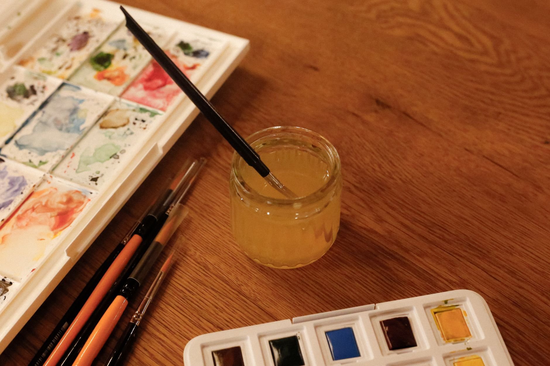 Close-up of watercolor palette and brushes on a wooden table, perfect for artistic needs